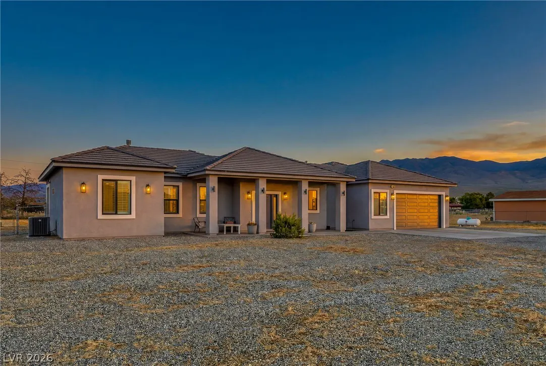 Single-story gray stucco home with a gravel yard and attached garage at sunset, set against a mountain backdrop.