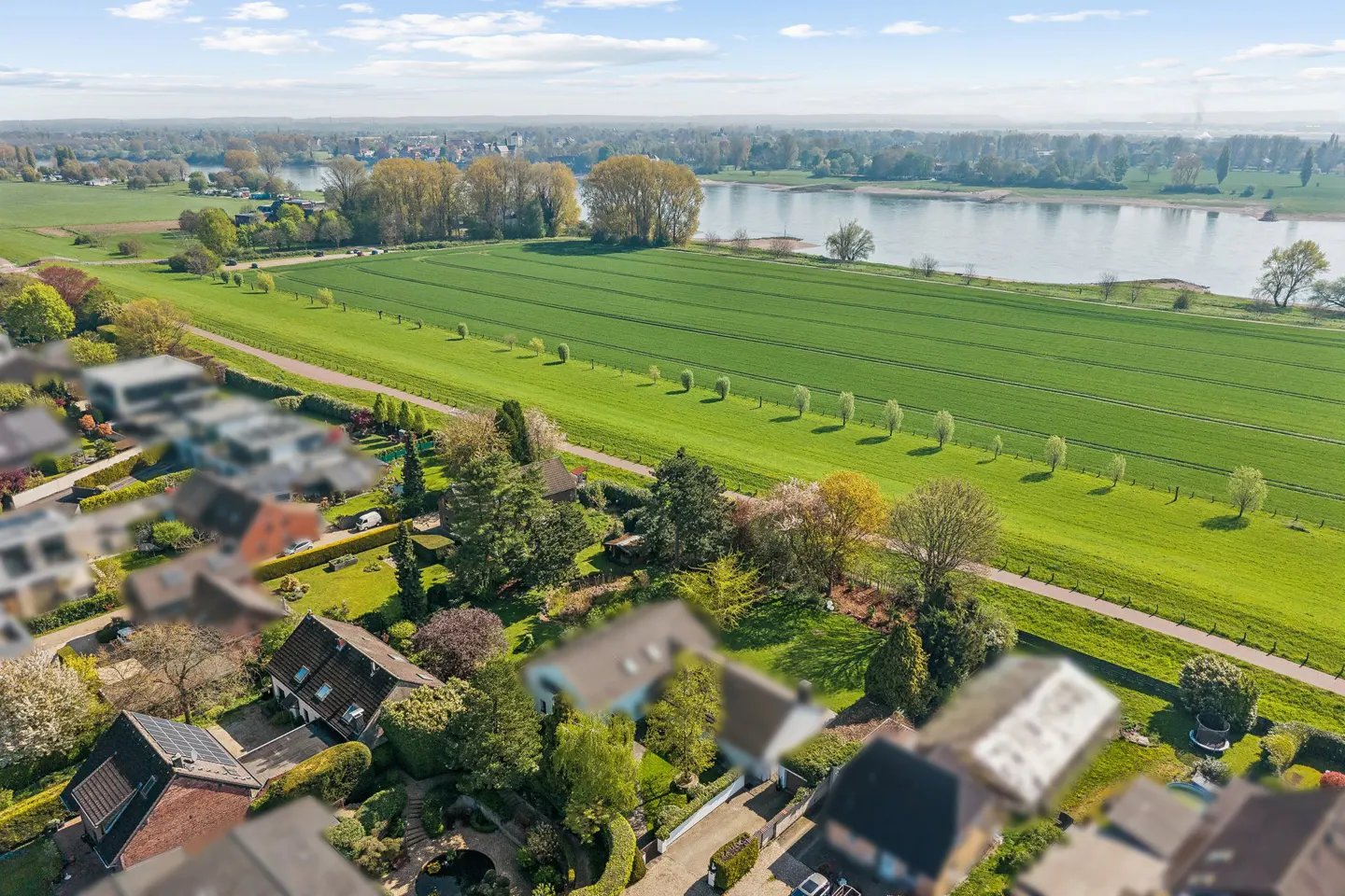 Aerial view of houses near a green field and river under a blue sky with white clouds.