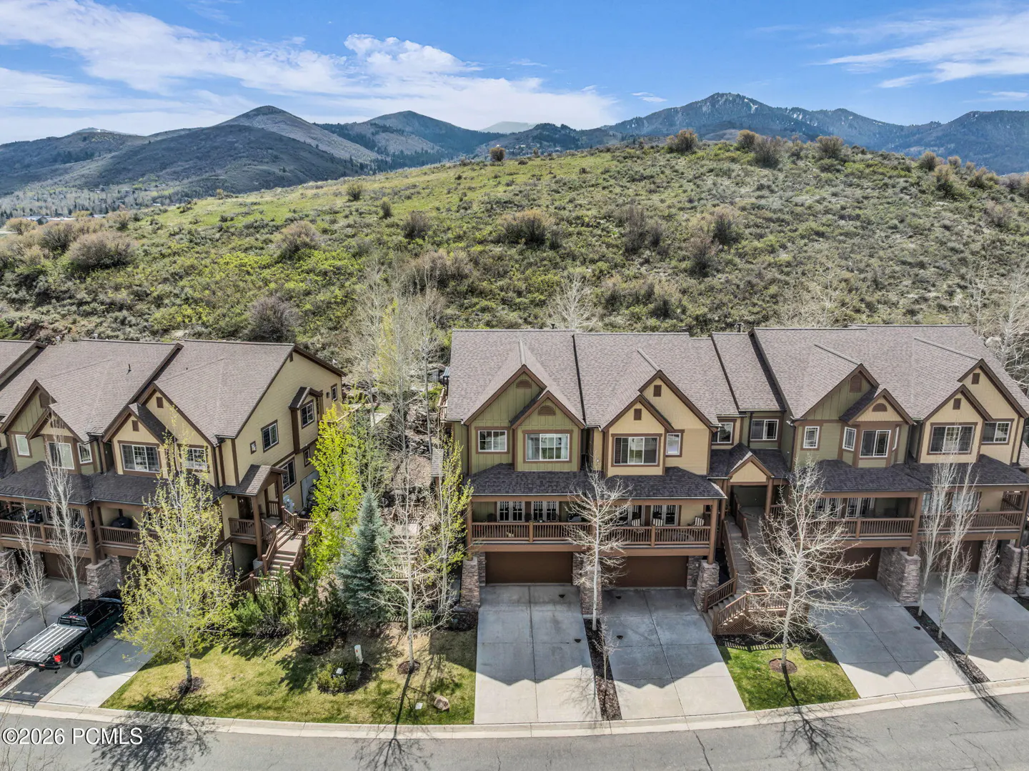 Aerial view of townhouses with brown roofs, beige and green siding, garages, and mountain backdrop.