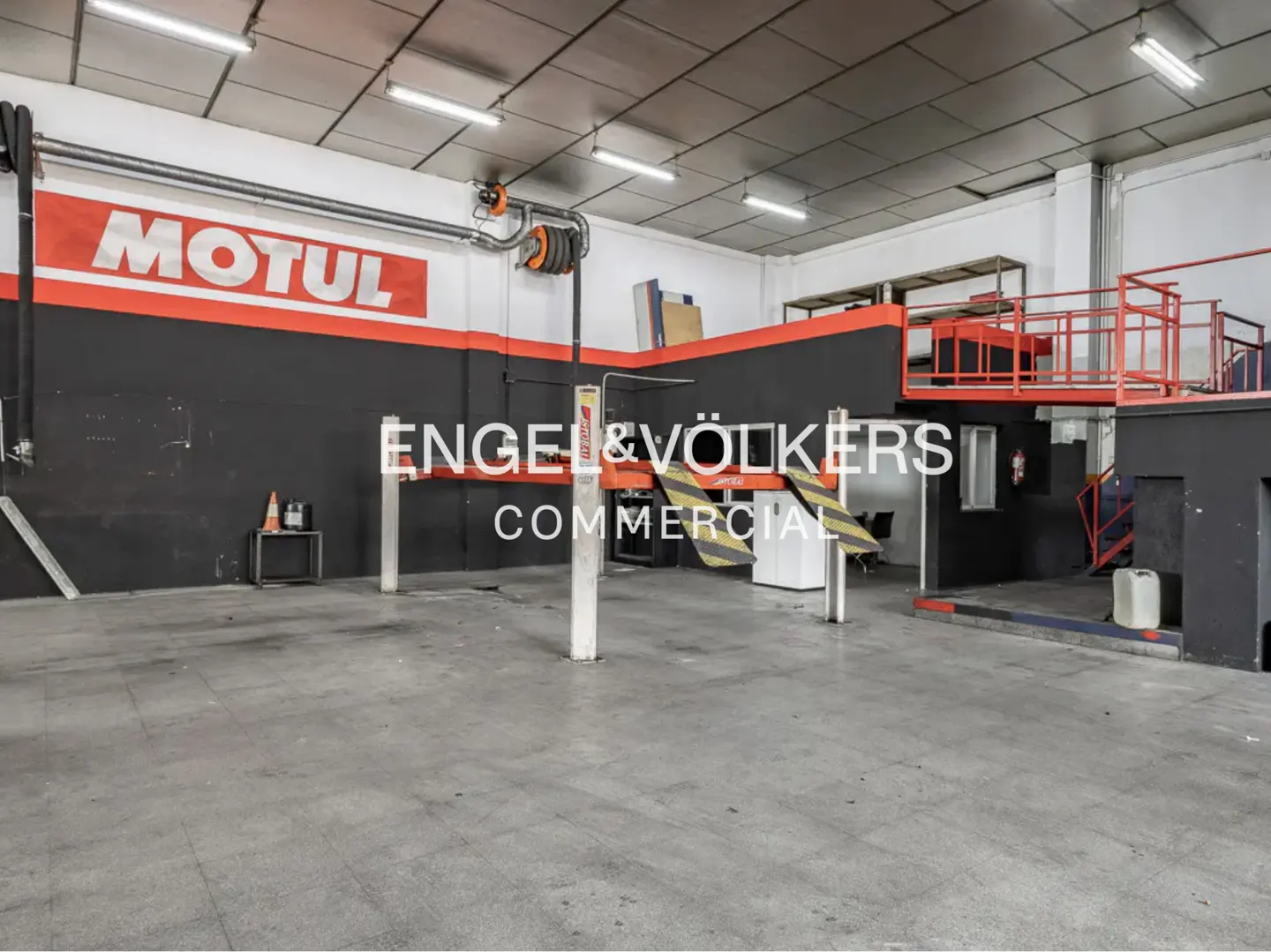 An empty auto repair shop with a car lift, gray floors, and a black and white wall with a red stripe.
