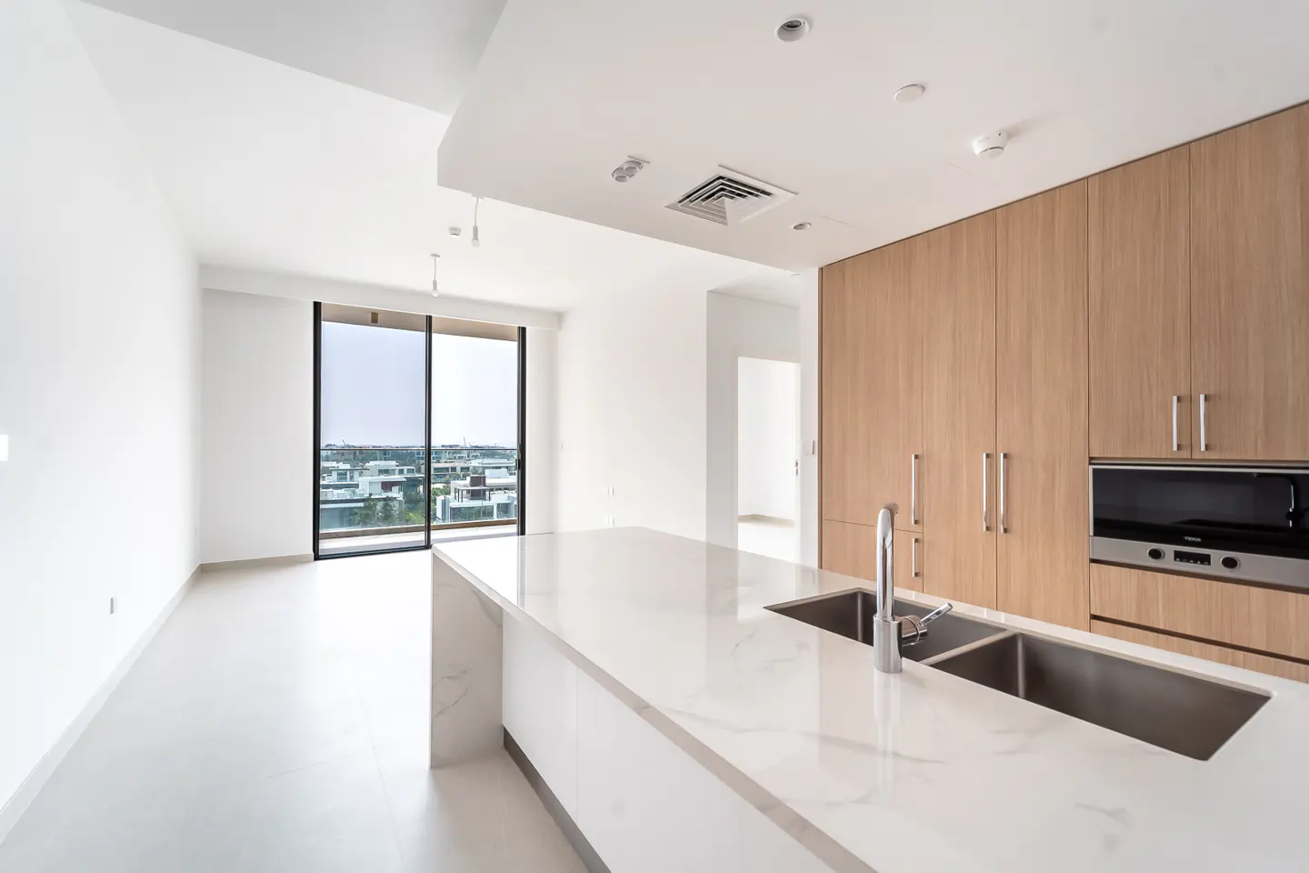 Bright, modern kitchen with white marble island, stainless steel sink, and wood cabinets. Large window overlooks a cityscape.