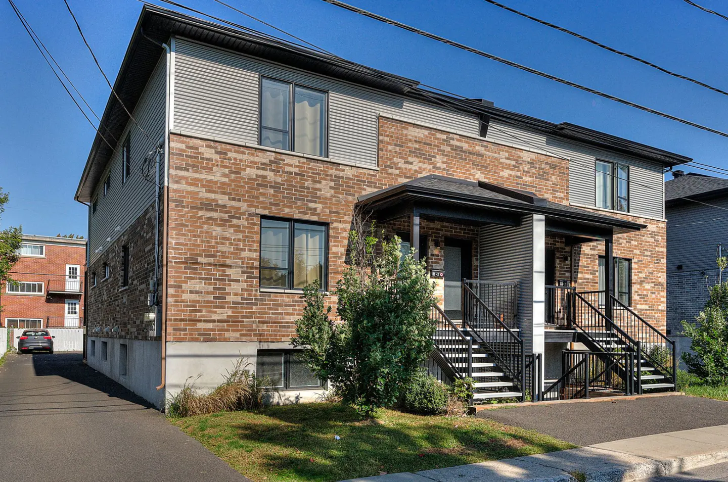 Exterior view of a two-story duplex with brick and gray siding, black stairs, and a small front yard.