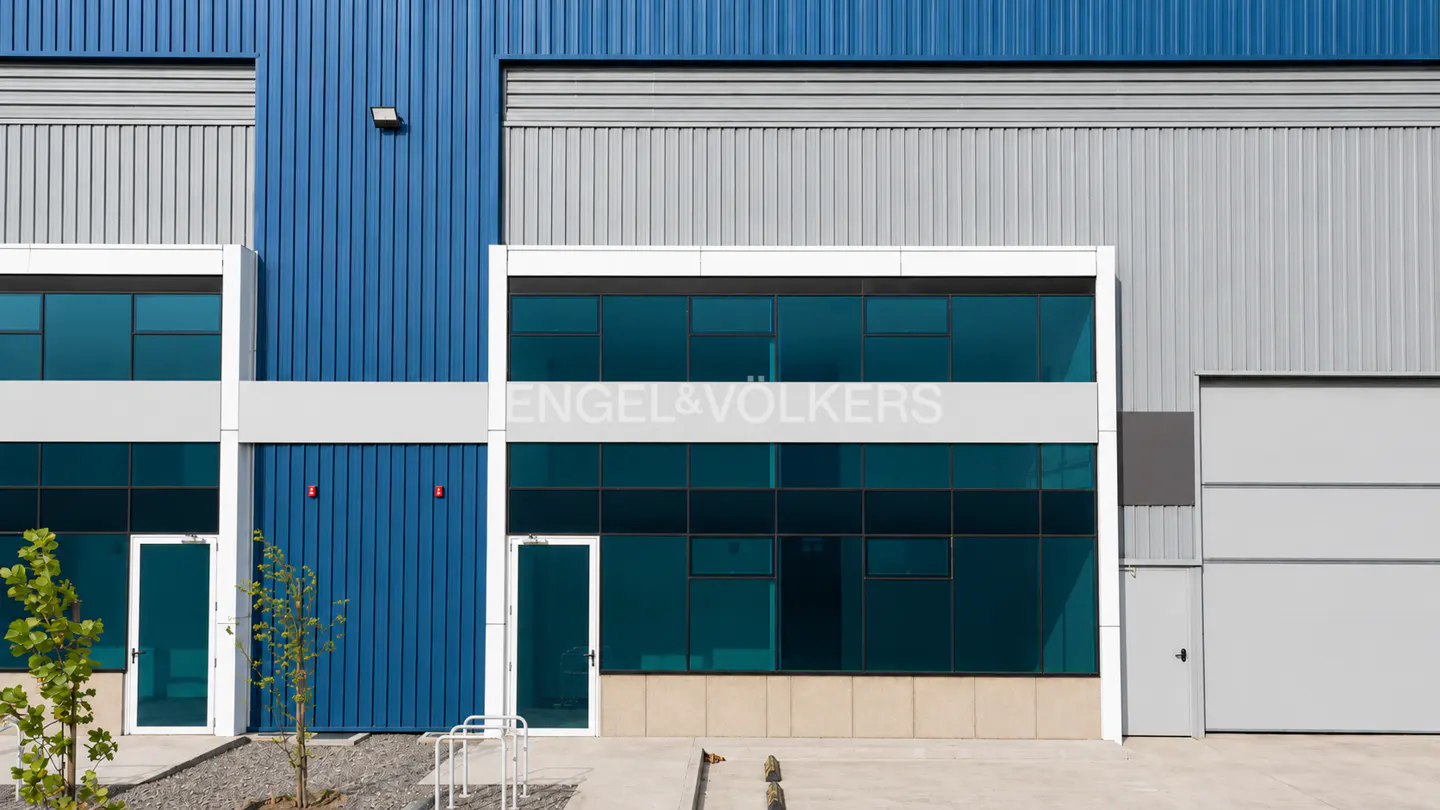 Exterior of a blue and gray commercial building with the Engel & Völkers logo on a white band above dark-tinted windows.