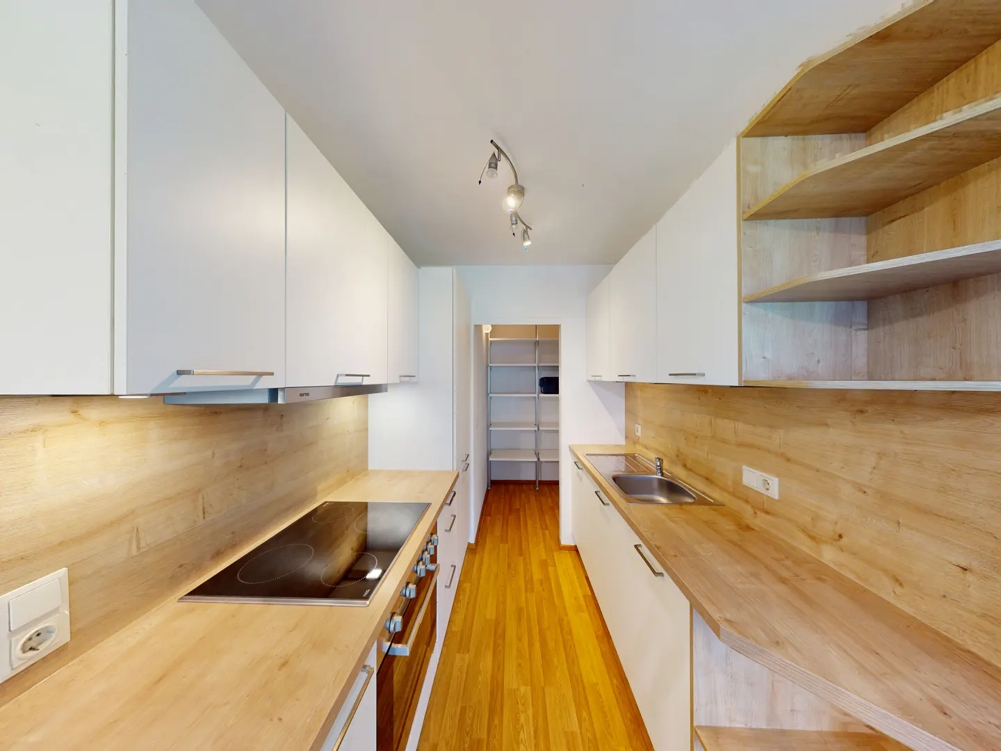 A modern kitchen with white cabinets, wood countertops, and a stainless steel sink. A pantry is visible in the background.
