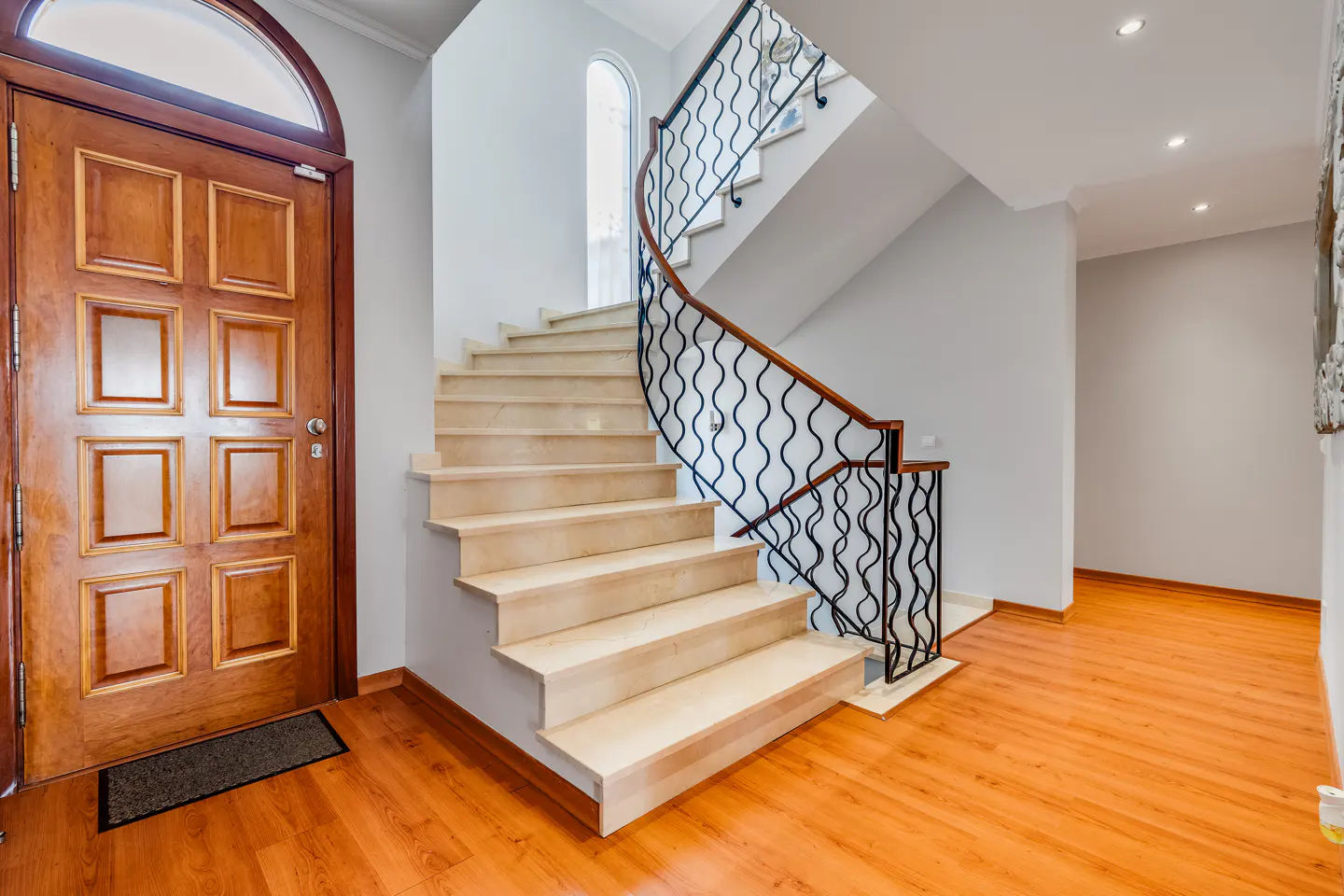 Entryway with a wooden door, marble staircase with black wrought iron railing, and hardwood floors.