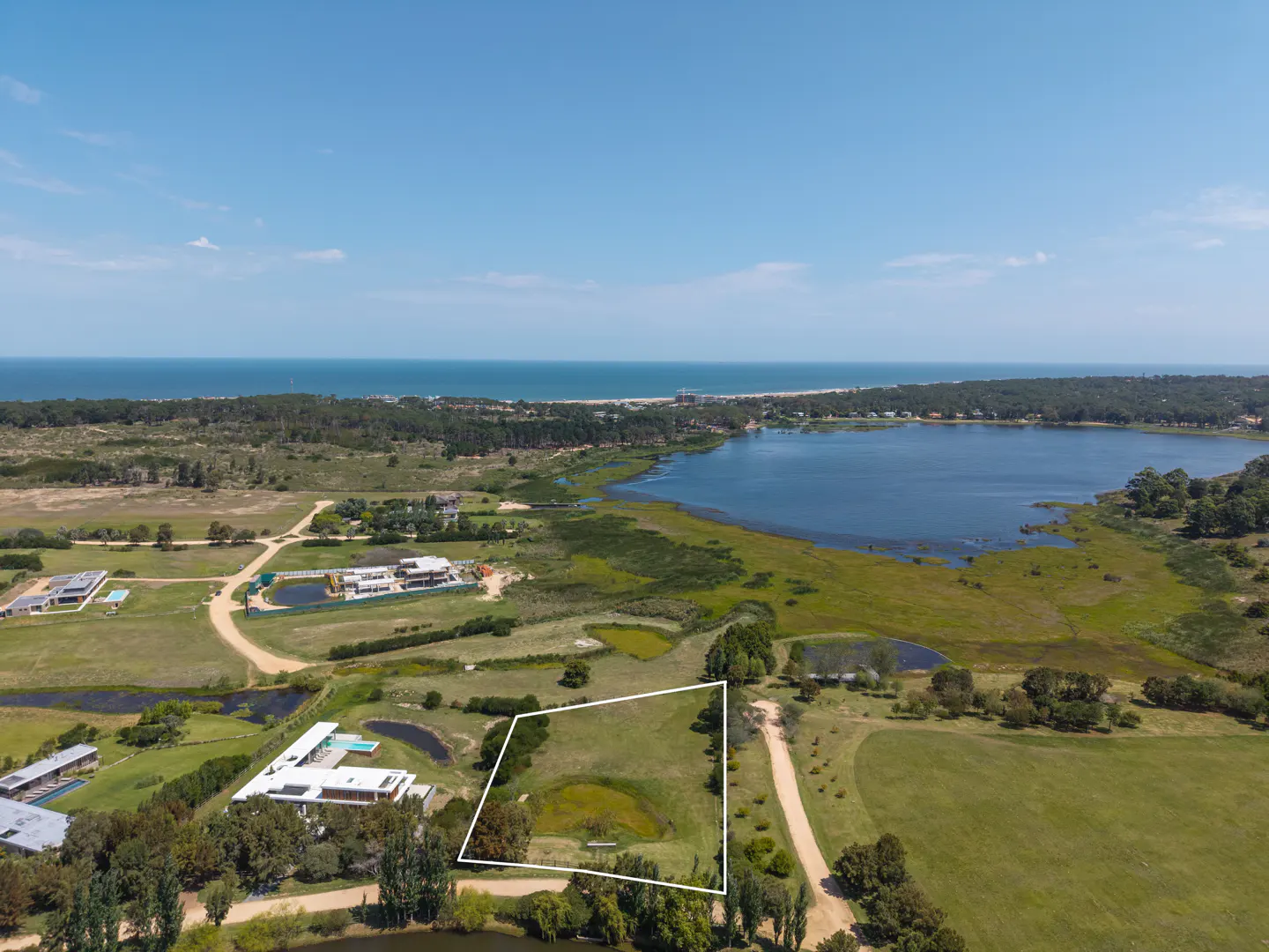 Aerial view of a vacant lot outlined in white, near a lake and the ocean under a blue sky.