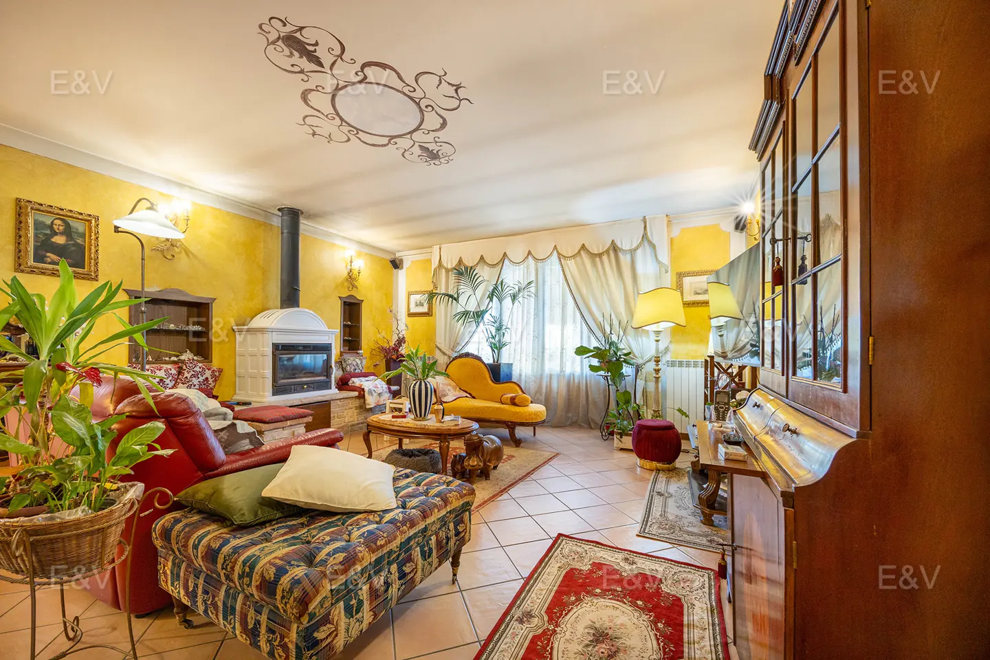 Cozy living room with yellow walls, a red leather sofa, patterned ottoman, fireplace, and ornate ceiling detail.