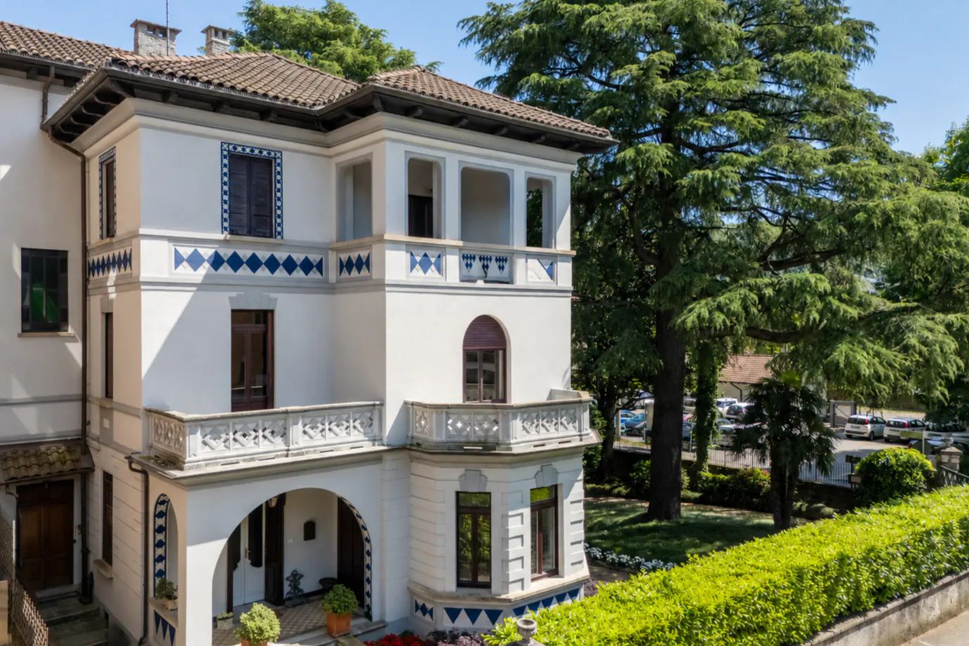 Exterior view of a three-story white building with blue diamond accents and a brown tile roof, surrounded by green trees.