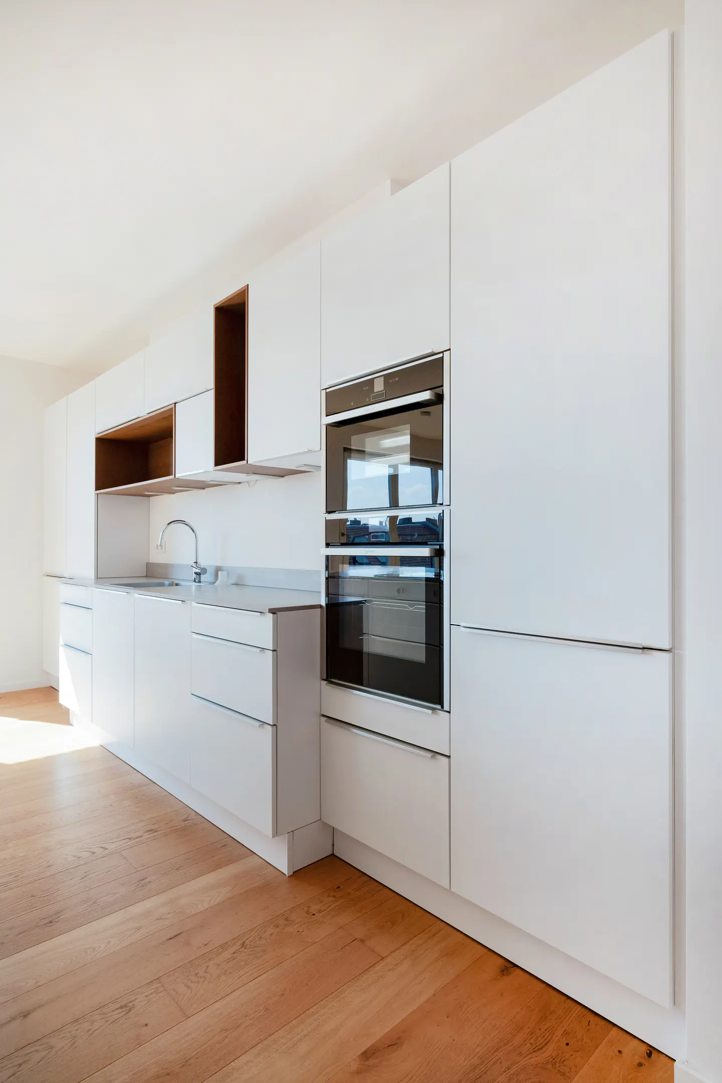 A modern kitchen with white cabinets, stainless steel appliances, and light wood floors.
