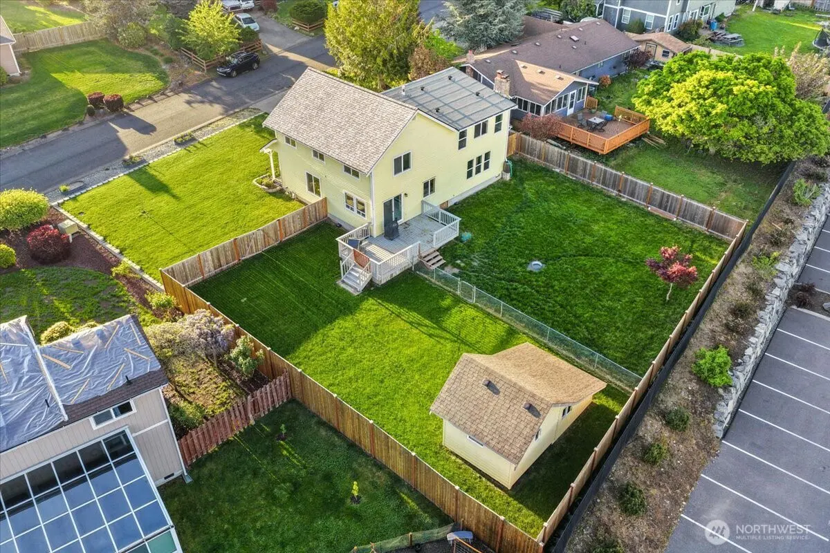 Aerial view of a yellow two-story house with a large, fenced backyard and a shed on a sunny day.