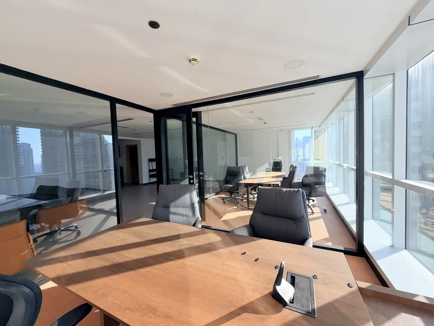 A modern office space with a large wooden conference table and gray chairs, glass walls, and city views.