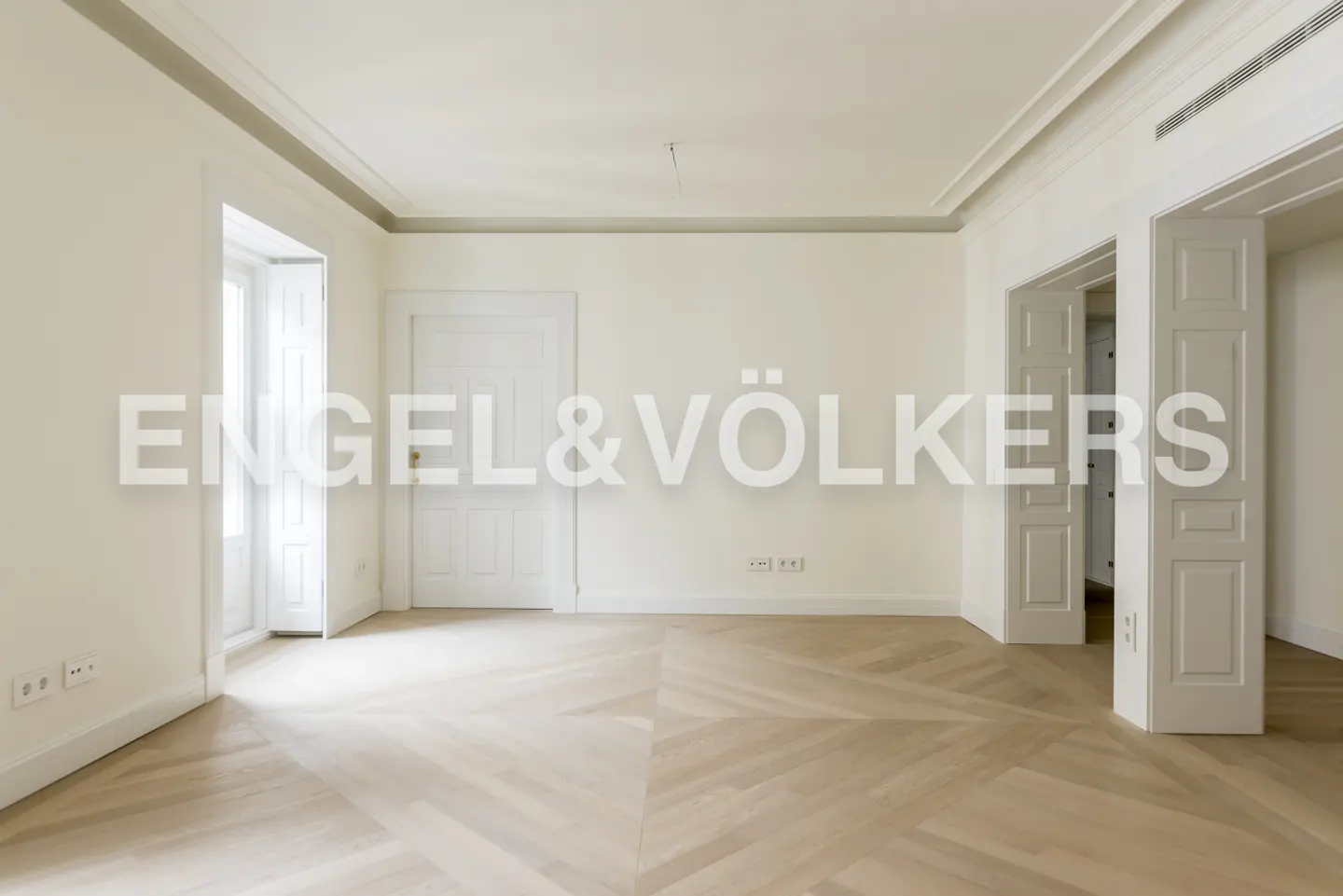 Empty room with herringbone wood floors, white walls, and white doors. Engel & Völkers logo overlayed.