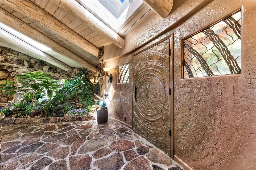 Entryway with stone floor, textured walls, a circular carved wooden door, skylights, and an indoor garden with plants.