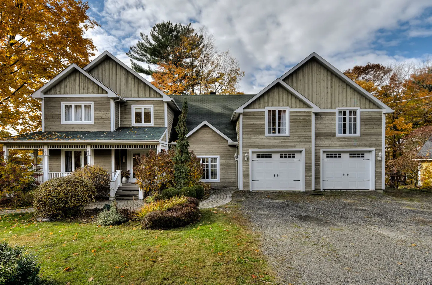 Two-story house with a green roof, light brown siding, white trim, and a two-car garage. Autumn trees surround the house.