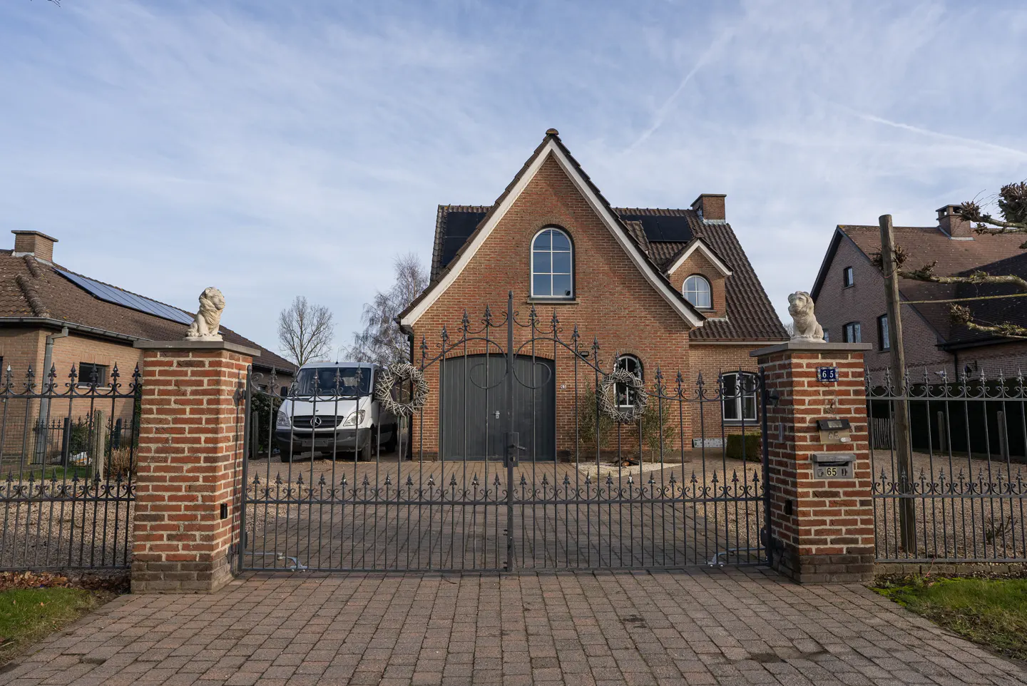 A brick house with a dark garage door behind a decorative iron gate, flanked by two brick pillars topped with lion statues.