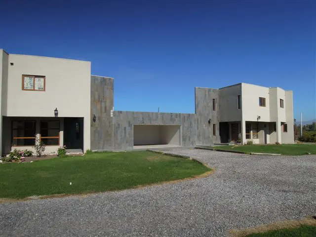 Modern beige house with a gray stone garage under a clear blue sky. A gravel driveway leads to the house.