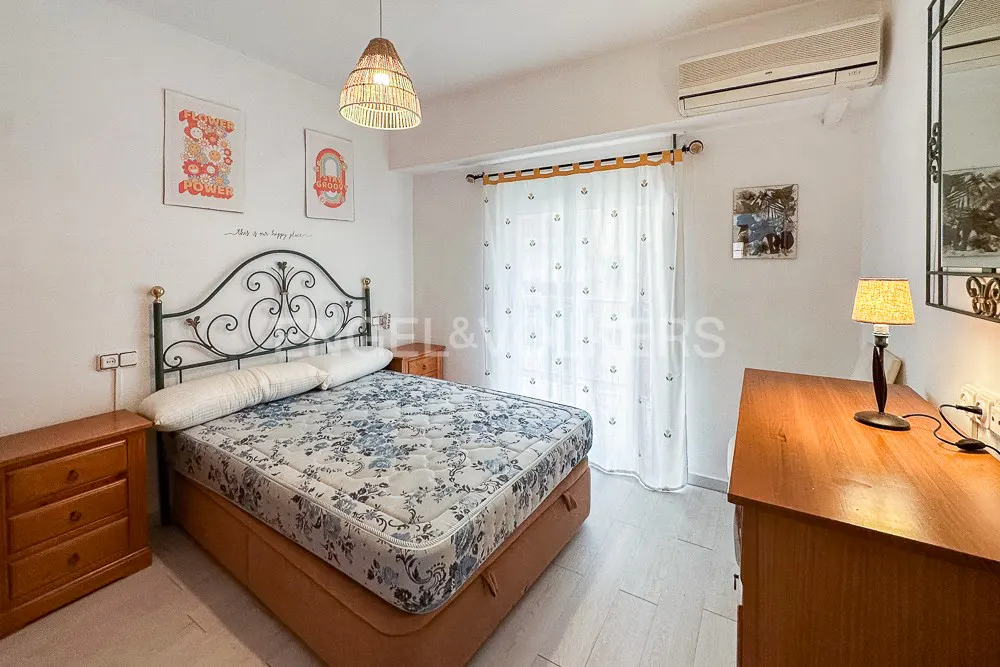 Bedroom with a floral bedspread, wrought iron headboard, wooden nightstands, and a woven pendant light.