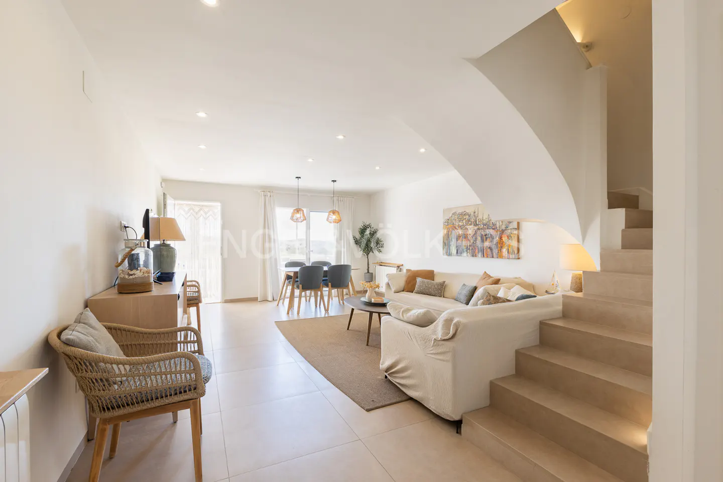 Bright, open-plan living space with dining table, sofa, and staircase. Neutral tones, natural light, and modern furnishings create a welcoming atmosphere.
