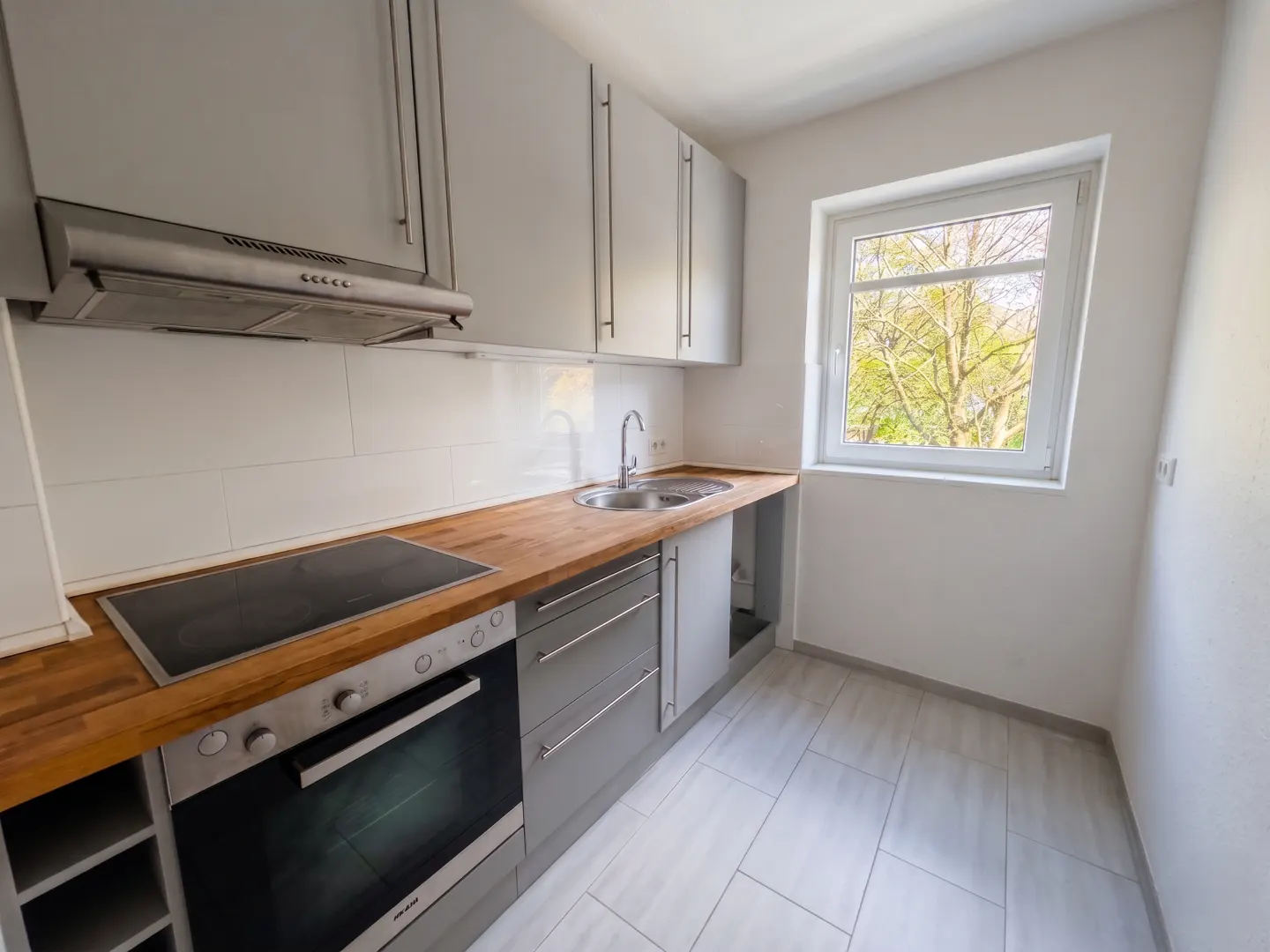 Bright kitchen with gray cabinets, wood countertops, stainless steel appliances, and a window with a tree view.