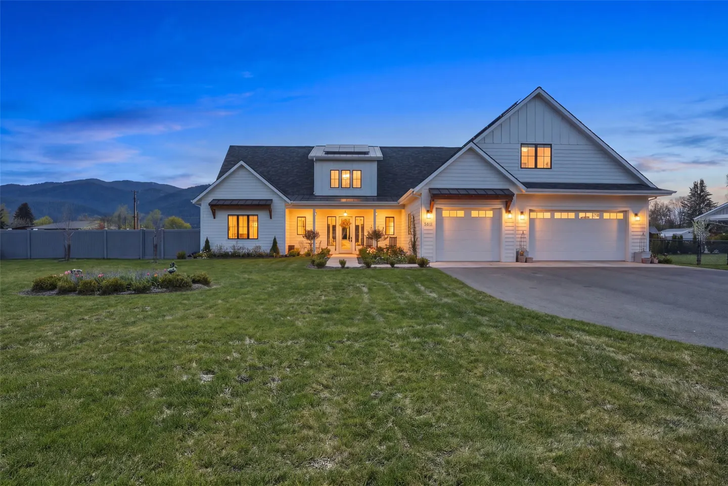 Two-story white farmhouse with a two-car garage, green lawn, and mountain backdrop at dusk.