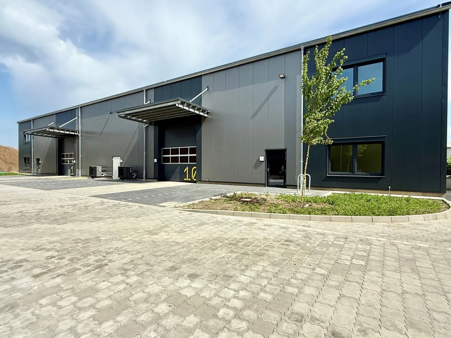 Exterior of a modern, gray industrial building with loading docks and a paved parking lot.