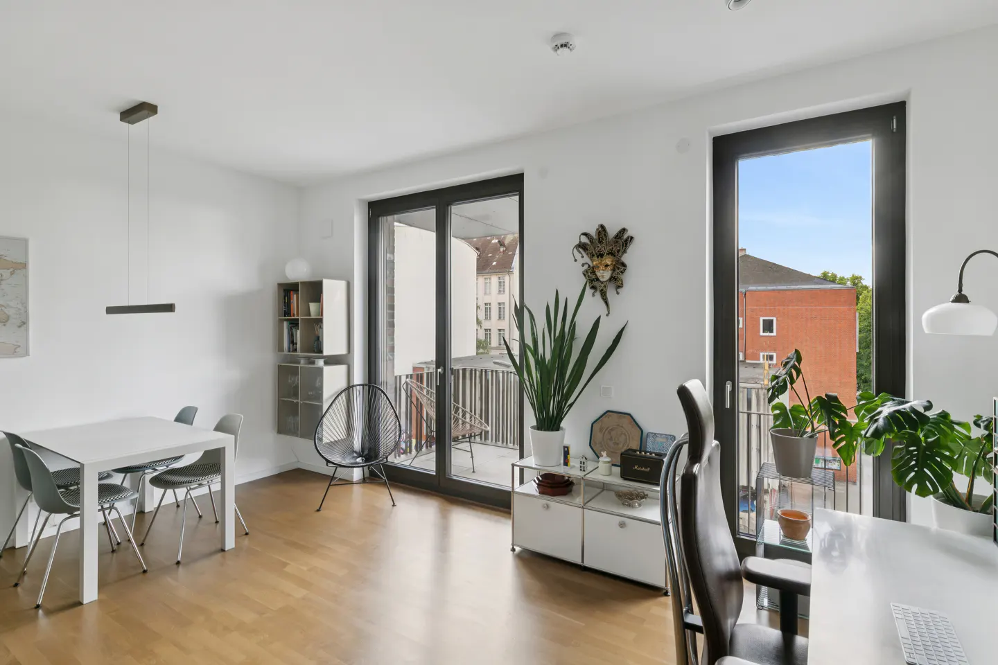 Bright, modern living room with dining area, office desk, hardwood floors, and balcony access with city views.