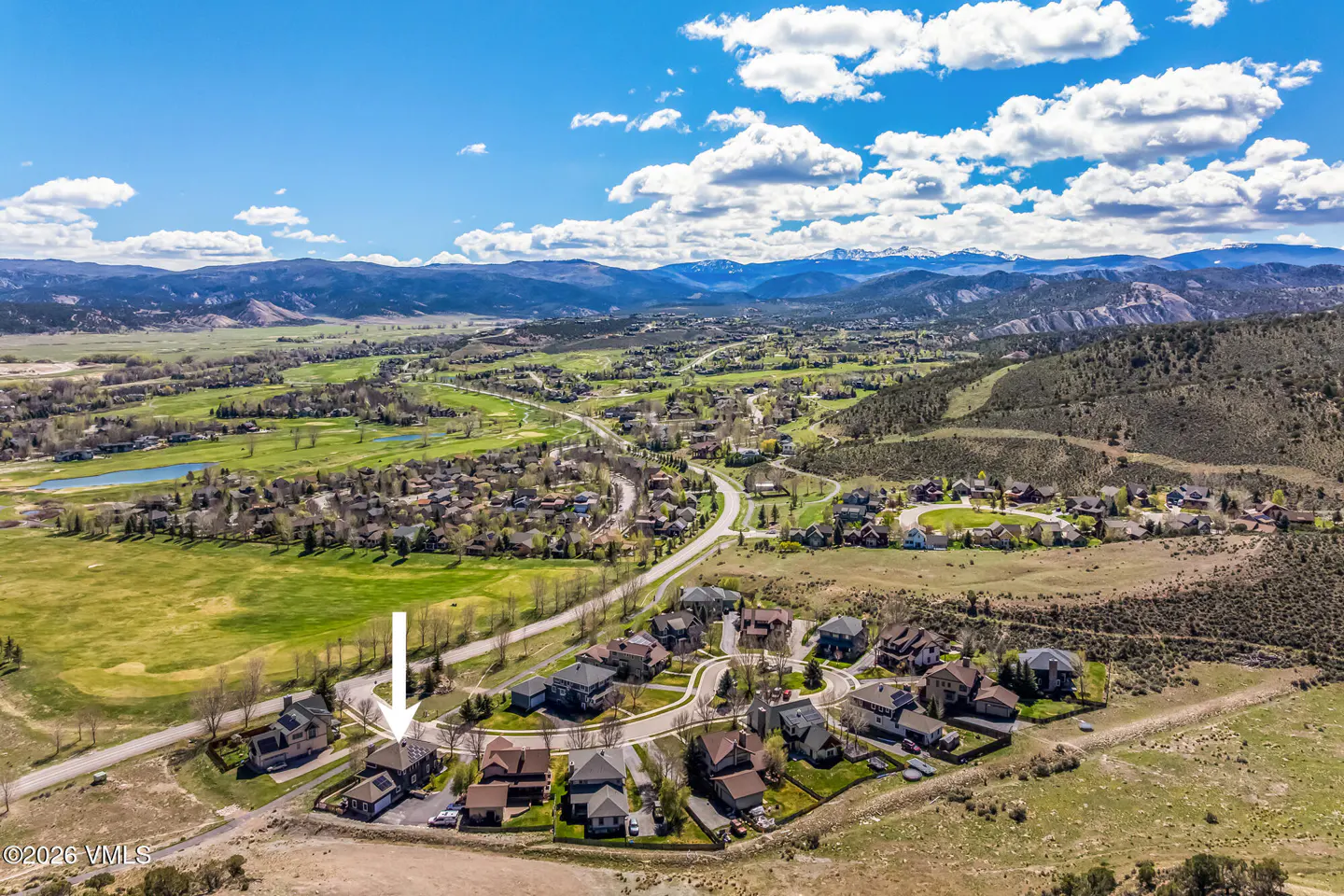 Aerial view of a neighborhood with an arrow pointing to a house, mountains in the background.