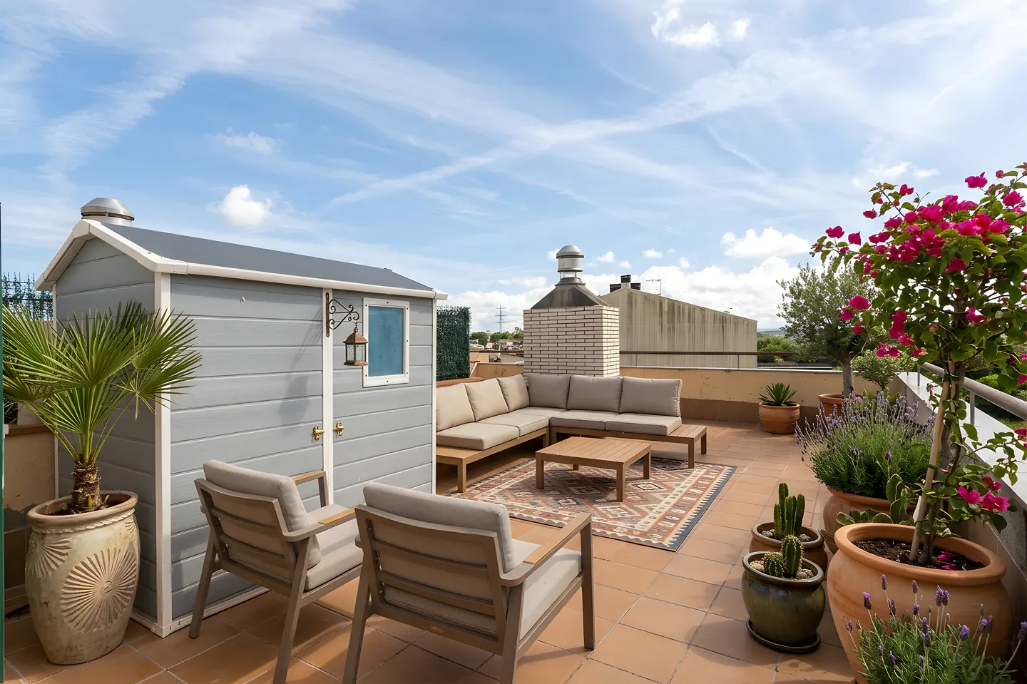 Rooftop patio with gray shed, seating area, and potted plants under a blue sky.