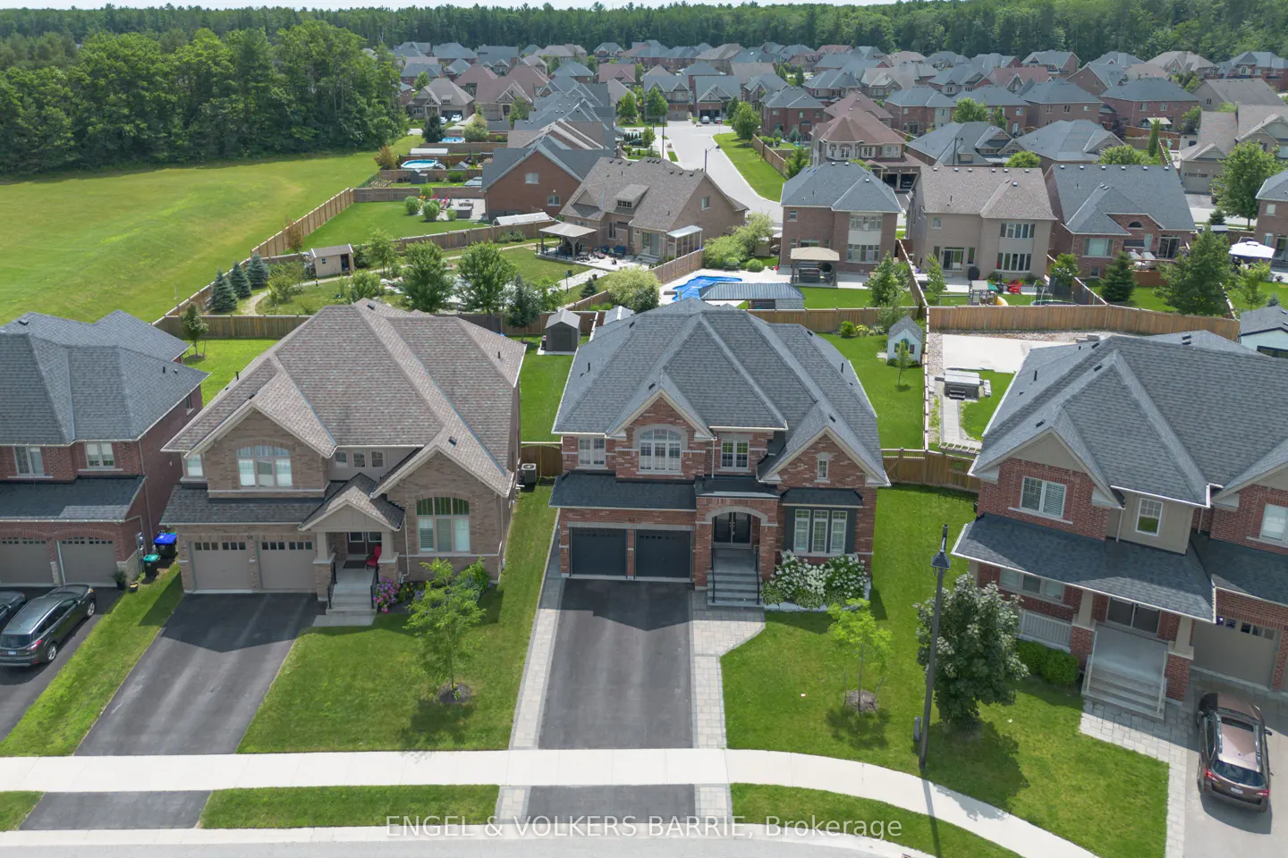 Aerial view of a suburban neighborhood with brick houses, green lawns, and a wooded area in the background.