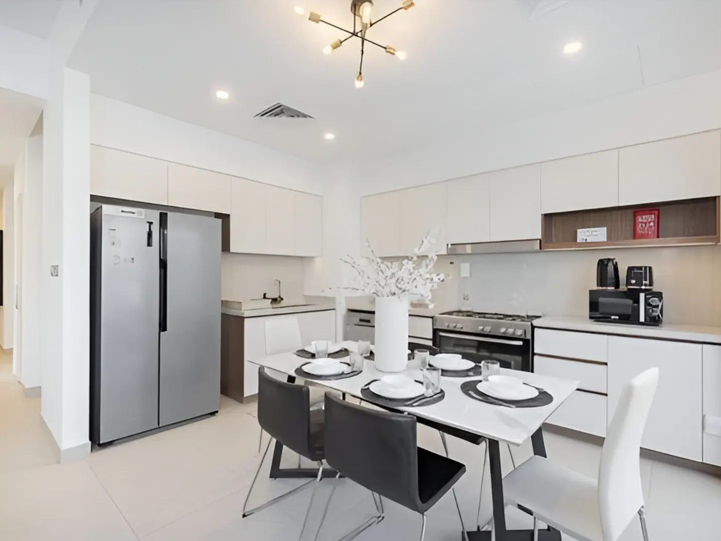 Modern kitchen with white cabinets, stainless steel fridge, and a dining table with black and white chairs.