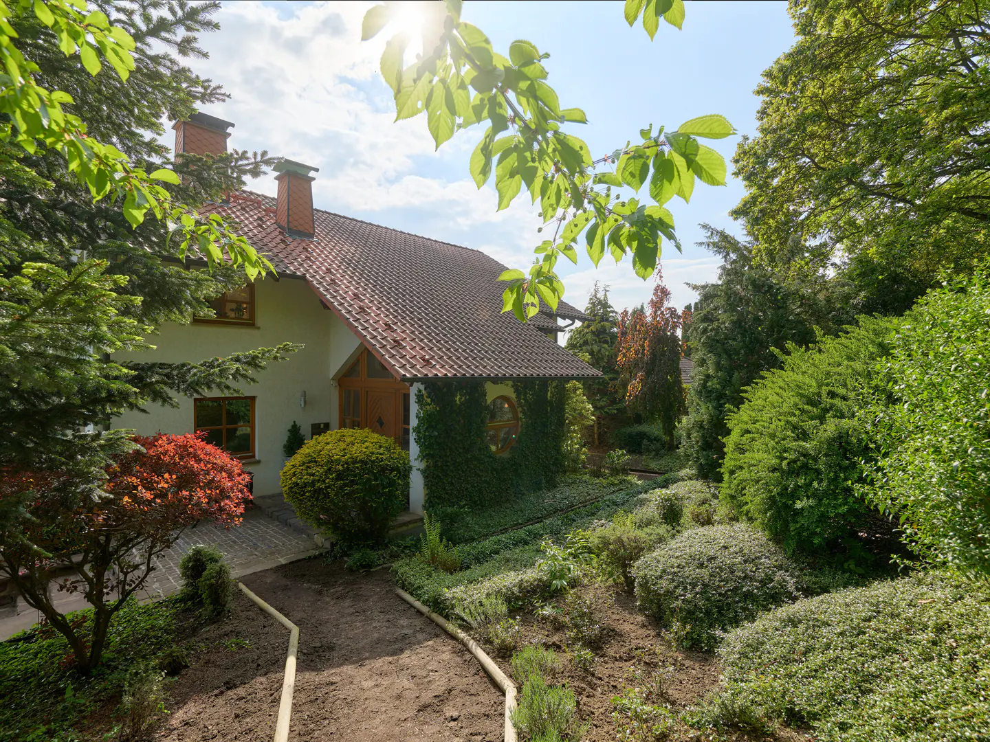 Exterior view of a white house with a red tile roof, surrounded by lush green trees and landscaping.