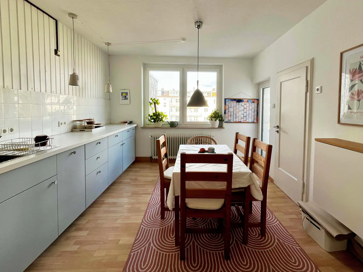 Bright kitchen with blue cabinets, white countertops, and a wooden dining table with chairs on a patterned rug.