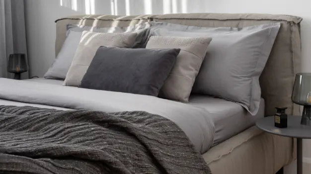 Bedroom with a bed with gray sheets, pillows, and a throw blanket. A gray nightstand is on the right.