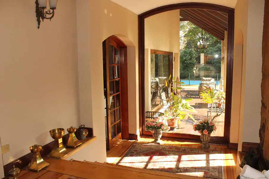Interior view of a home with arched doorways leading to a patio with a pool and seating. Vases of flowers and potted plants are visible.