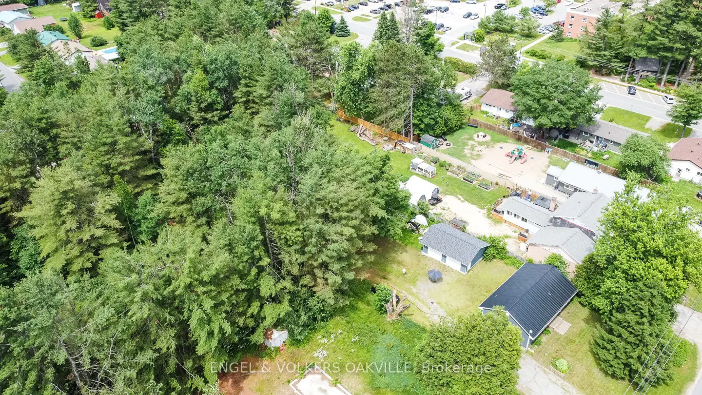 Aerial view of a wooded residential area with houses, a playground, and a parking lot in the background.