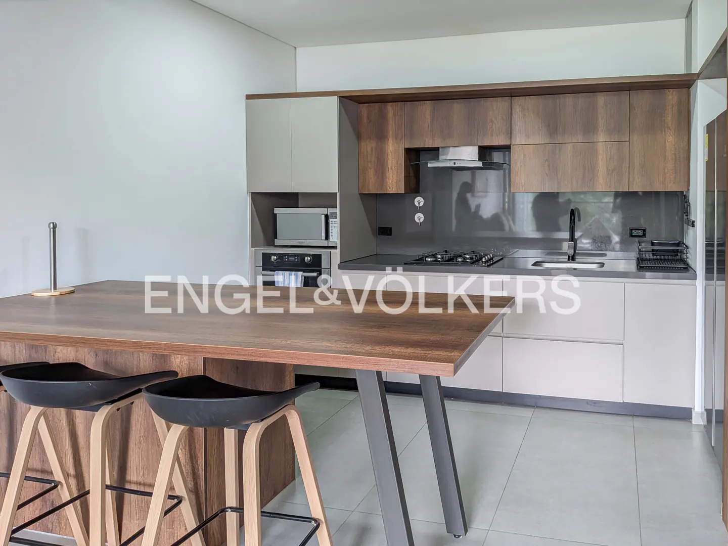 A modern kitchen with wood cabinets, gray countertops, and a large island with black stools.