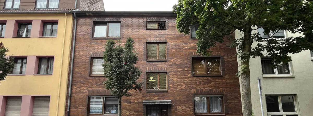 A three-story brick apartment building with many windows and trees in front.