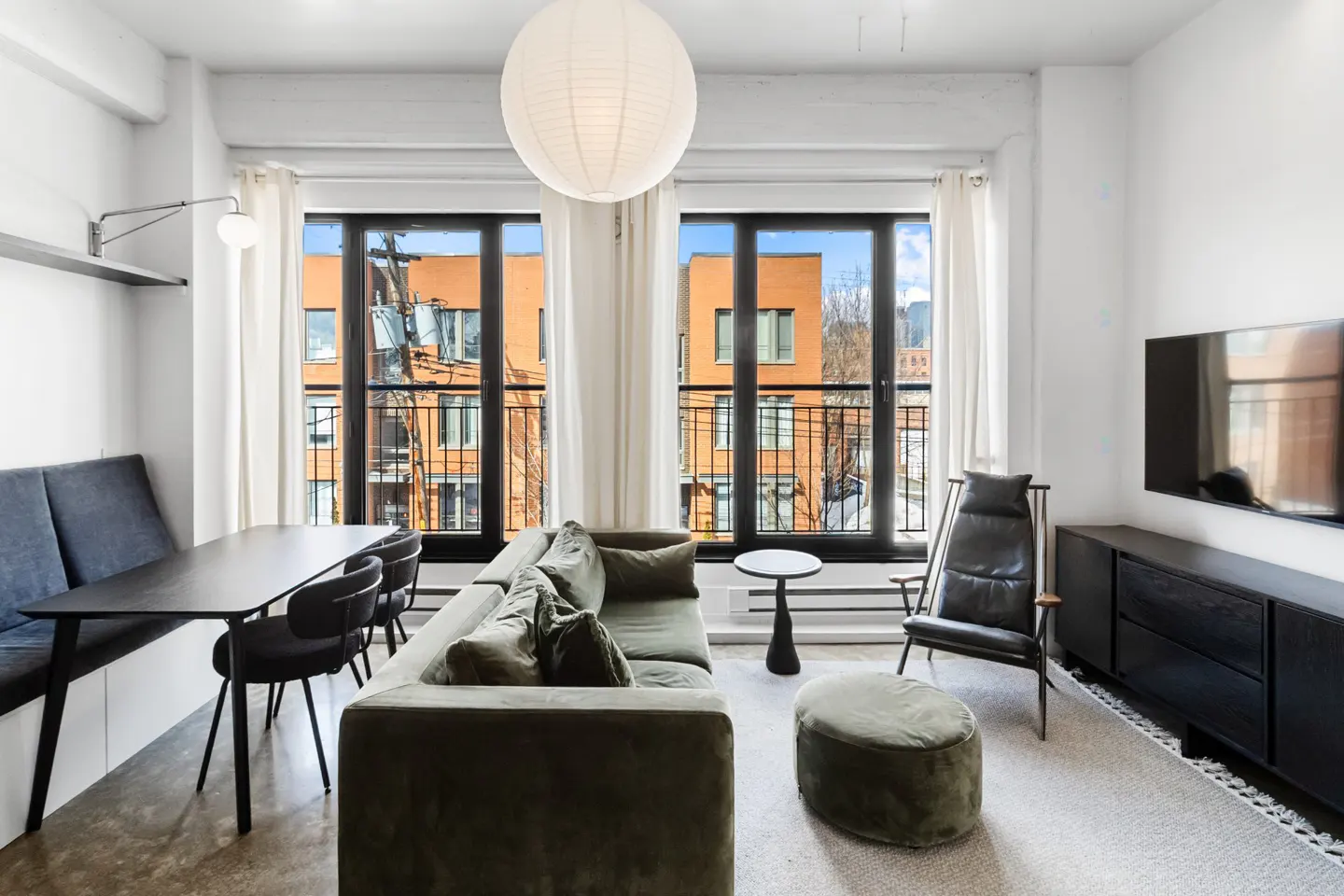 Bright living room with a green sofa, black dining table, and a large window with a view of an orange building.
