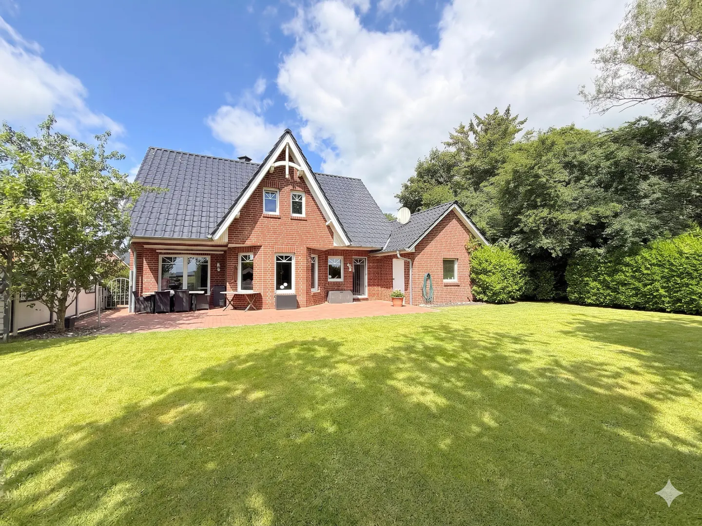 Red brick house with a dark roof and green lawn under a blue sky with white clouds.