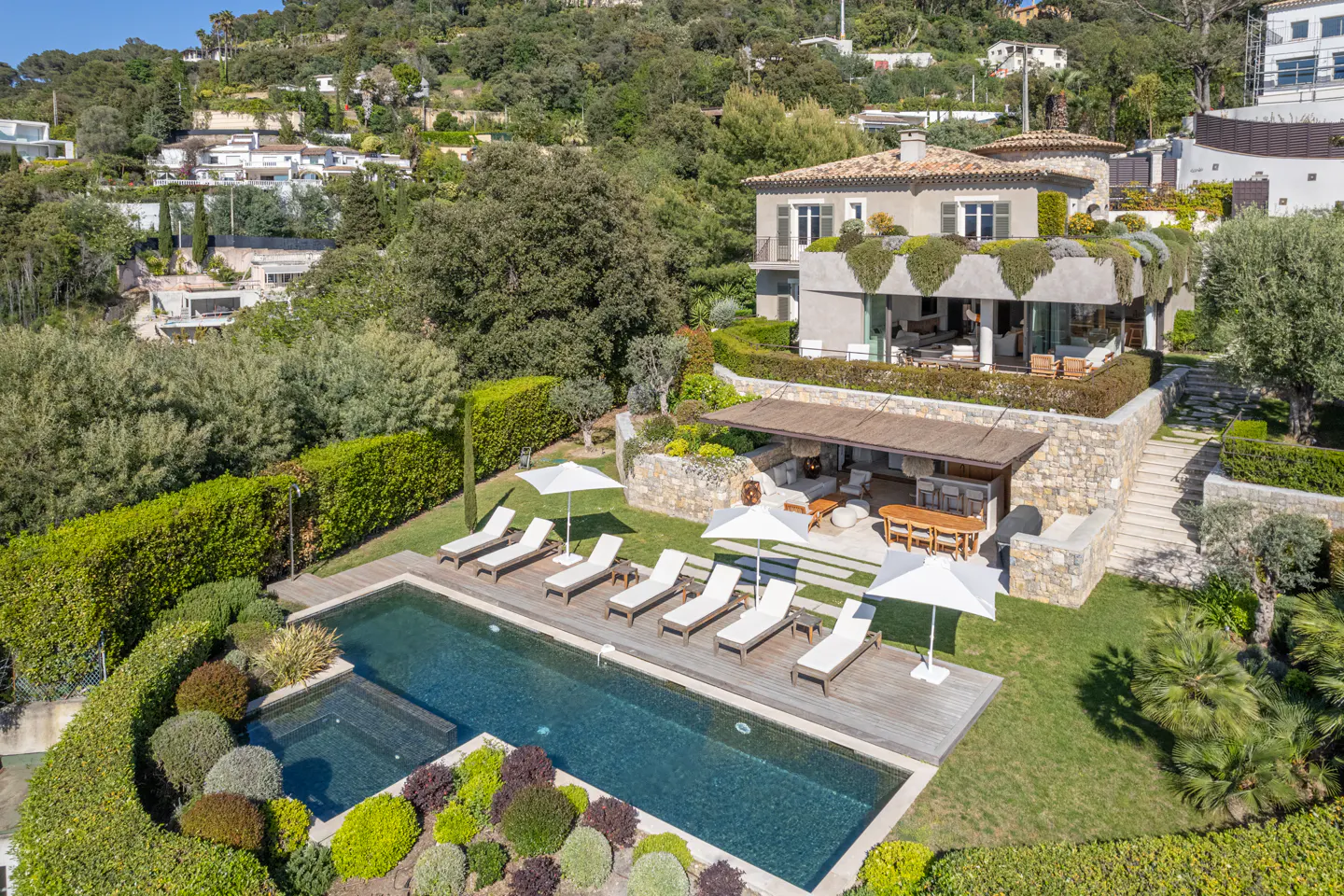 Aerial view of a luxury home with a pool, lounge chairs, and lush green landscaping on a hillside.