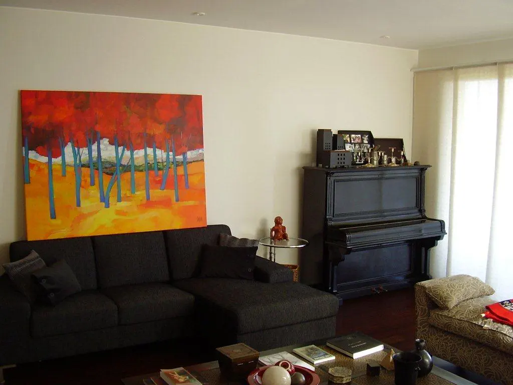 Living room with a dark gray sectional sofa, a colorful painting, and a black upright piano.