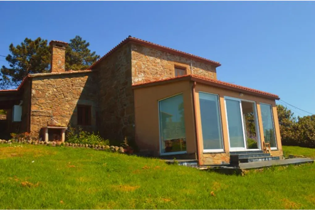 A two-story stone house with a red tile roof and a sunroom addition on a green lawn.