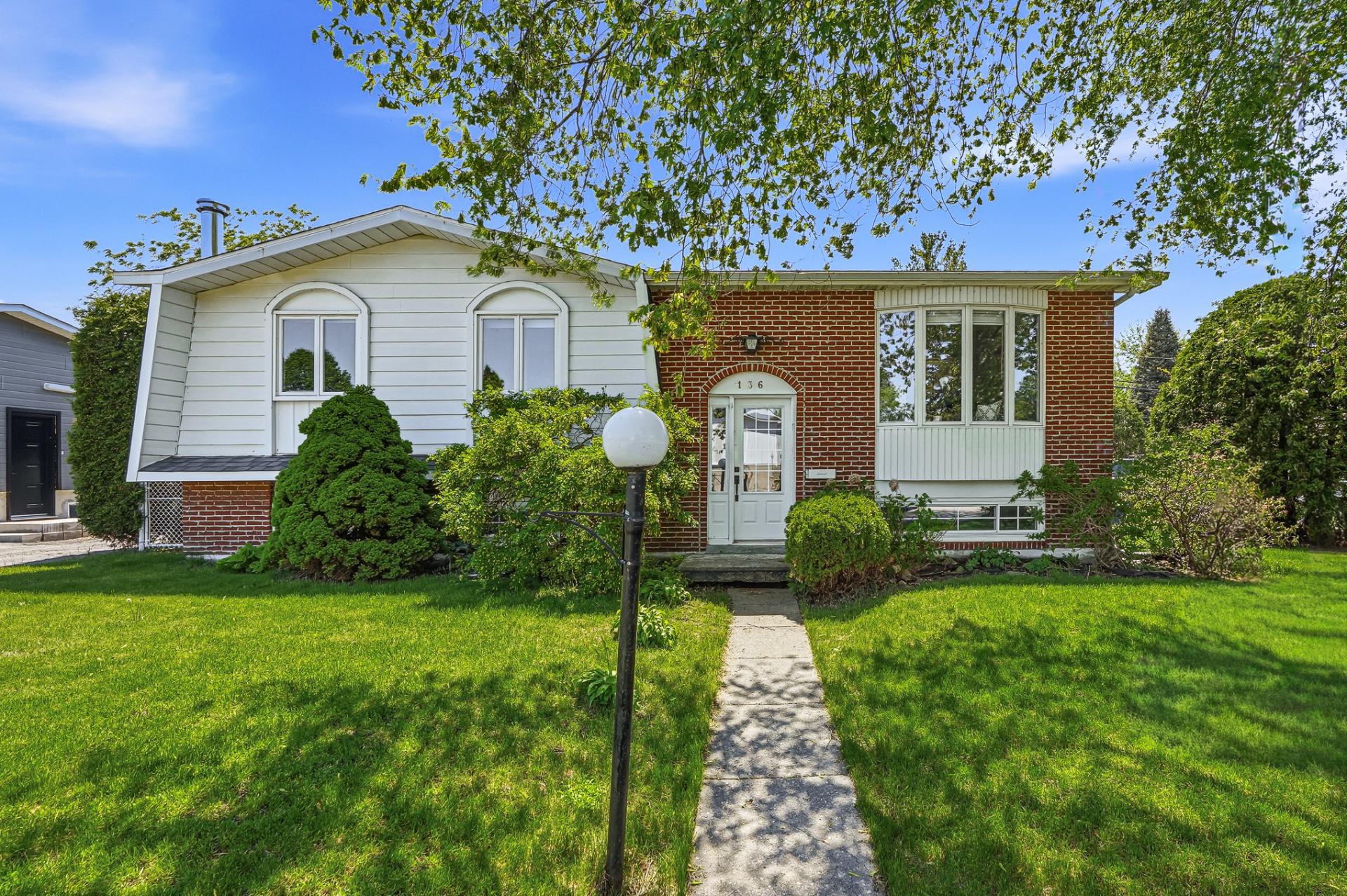 Two-story house with white siding and brick facade, green lawn, and a concrete walkway leading to the white front door.