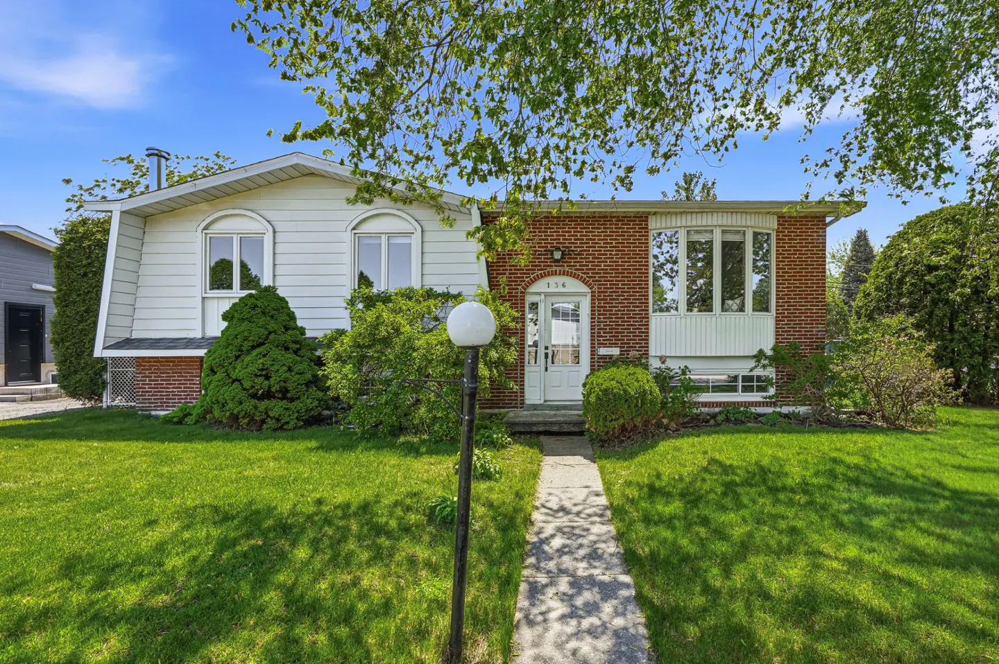 Two-story house with white siding and brick facade, green lawn, and a concrete walkway leading to the white front door.