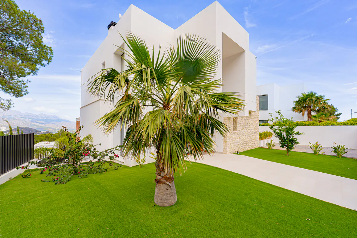 Modern white house with a palm tree in the front yard. Green grass and blue sky.