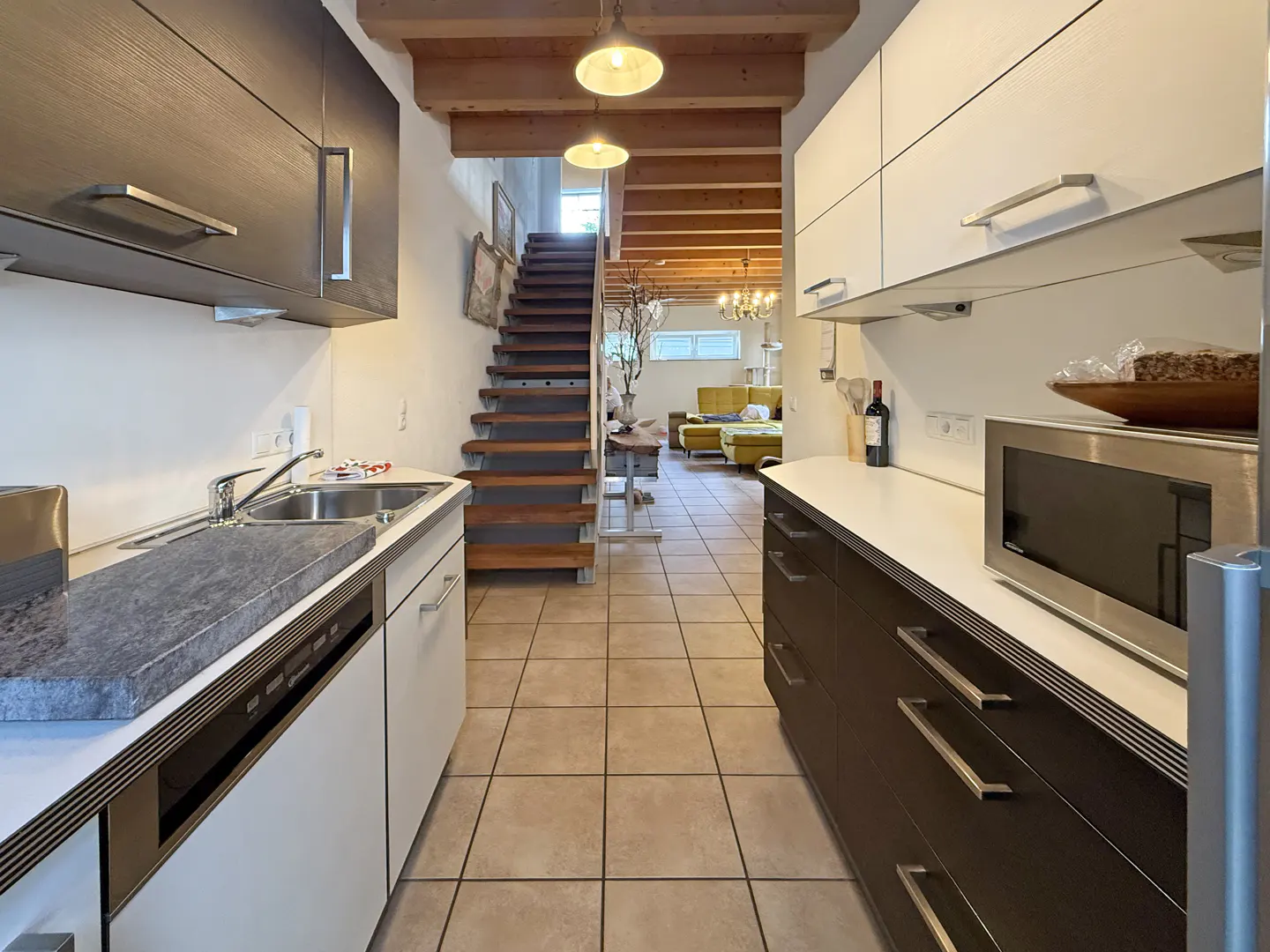 A kitchen with brown and white cabinets, stainless steel appliances, and a view of a staircase and living room.