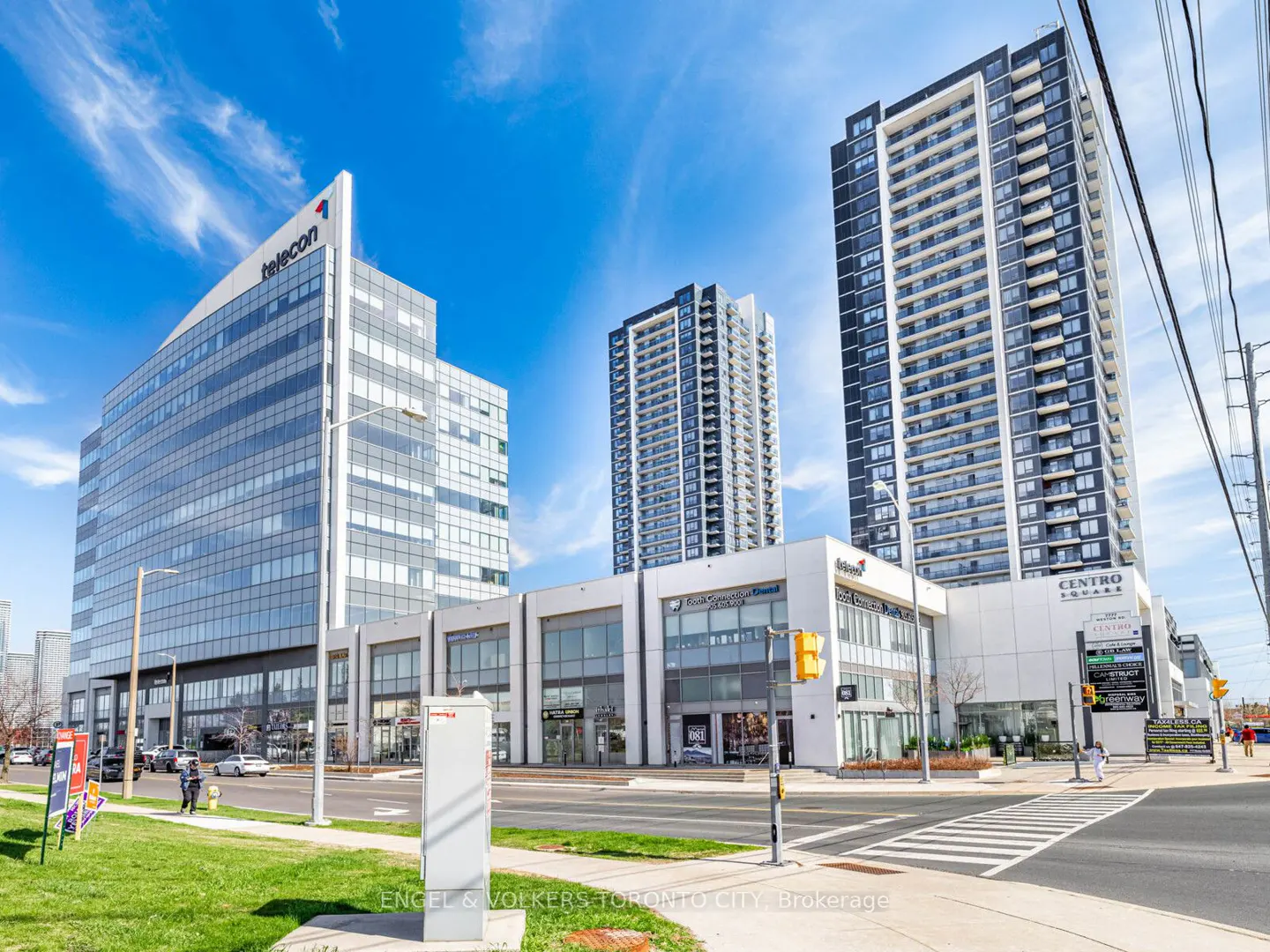 View of modern buildings, including a glass office tower with "telecon" logo, and residential high-rises under a blue sky.
