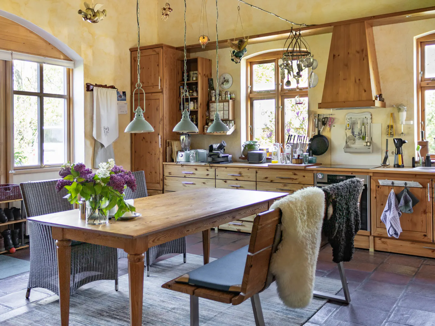 A rustic kitchen with wooden cabinets, a dining table with flowers, and natural light from windows.