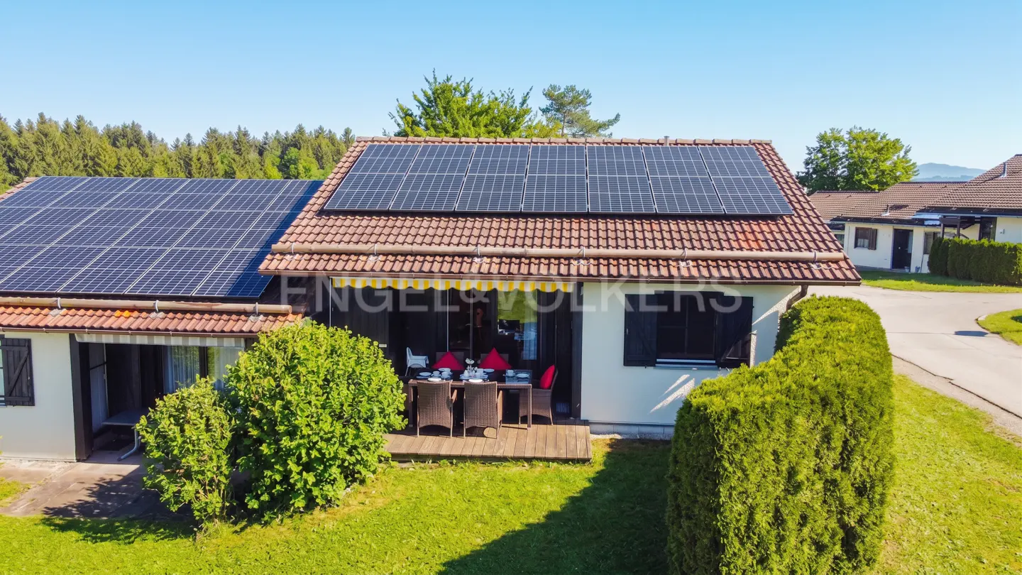 Aerial view of a house with solar panels on the roof, a wooden deck, and a green lawn.