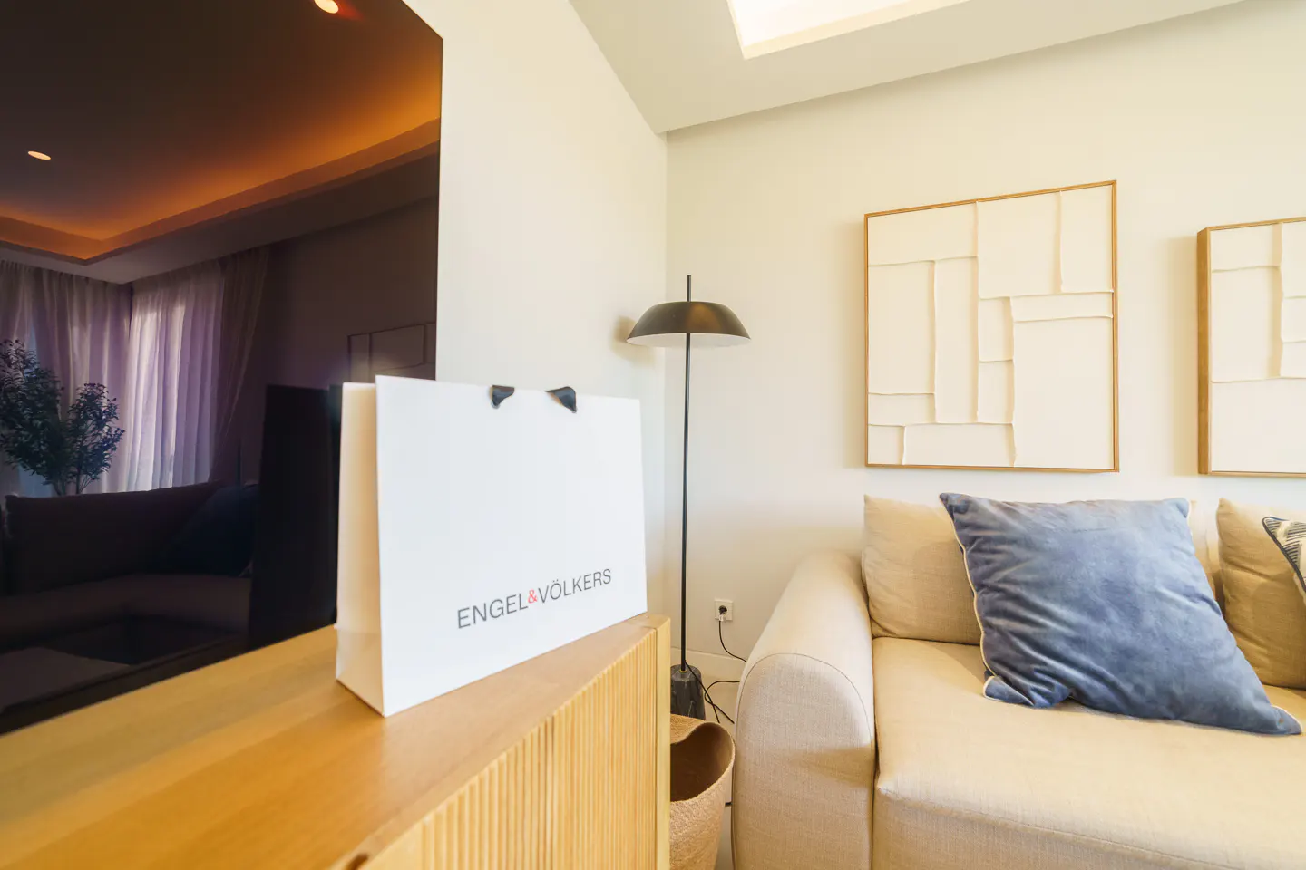 Living room with a white Engel & Völkers shopping bag on a wooden cabinet, a beige sofa, and modern art on the wall.